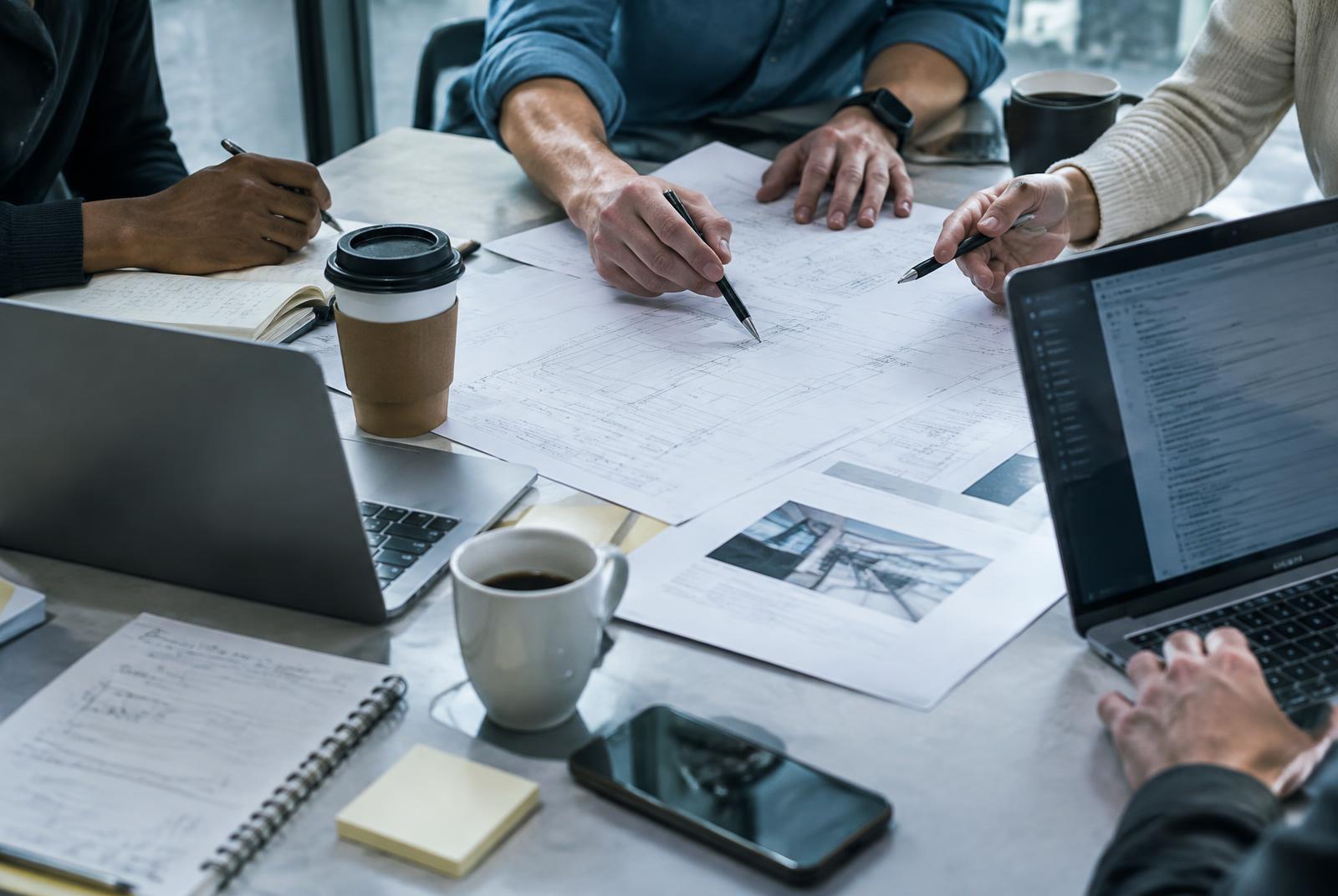 Hands of a team gathered over technical documents on a work table